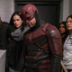 Luke Cage, Jessica Jones, Daredevil, Claire Temple, and Colleen Wing stand at the top of a white brick stairwell.